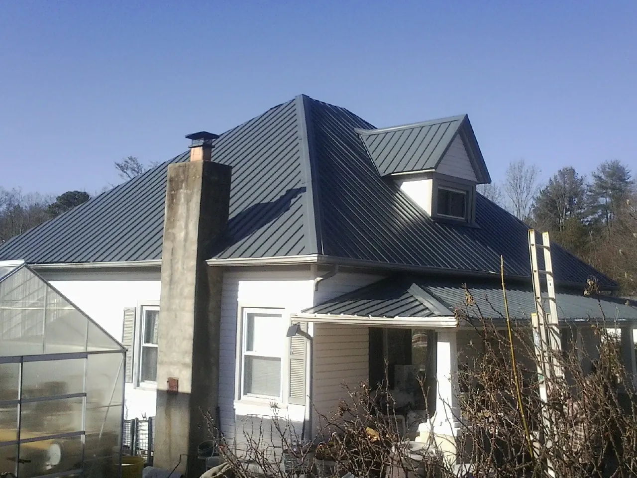 Dark blue standing seam metal roof on a white farmhouse with dormer — Slate & Tile Roof Repair by Roofing Brothers in Silvis