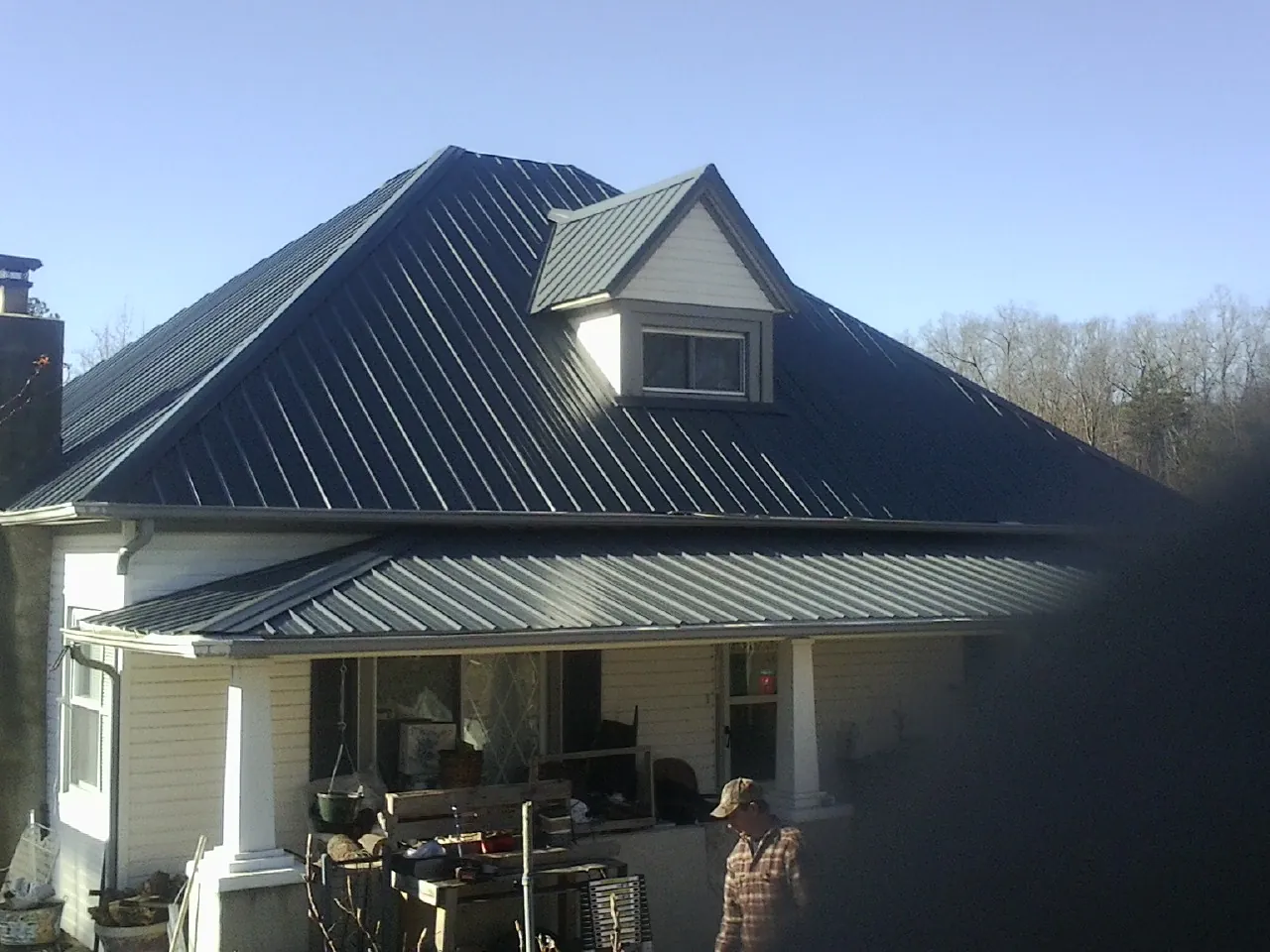 Dark blue standing seam metal roof with a dormer above a front porch in Silvis