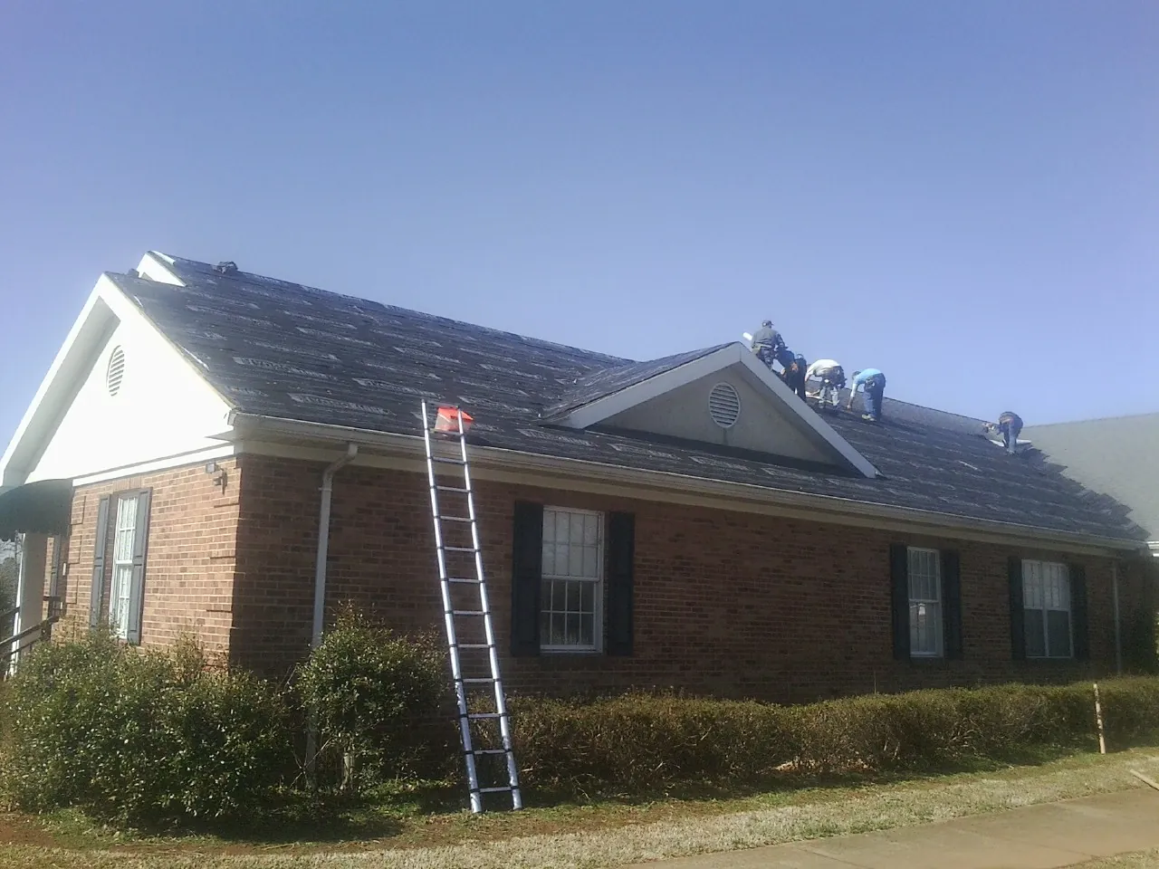 Crew tearing shingles off a brick ranch roof with a ladder set — Metal Roof Repair work by our crew in Silvis