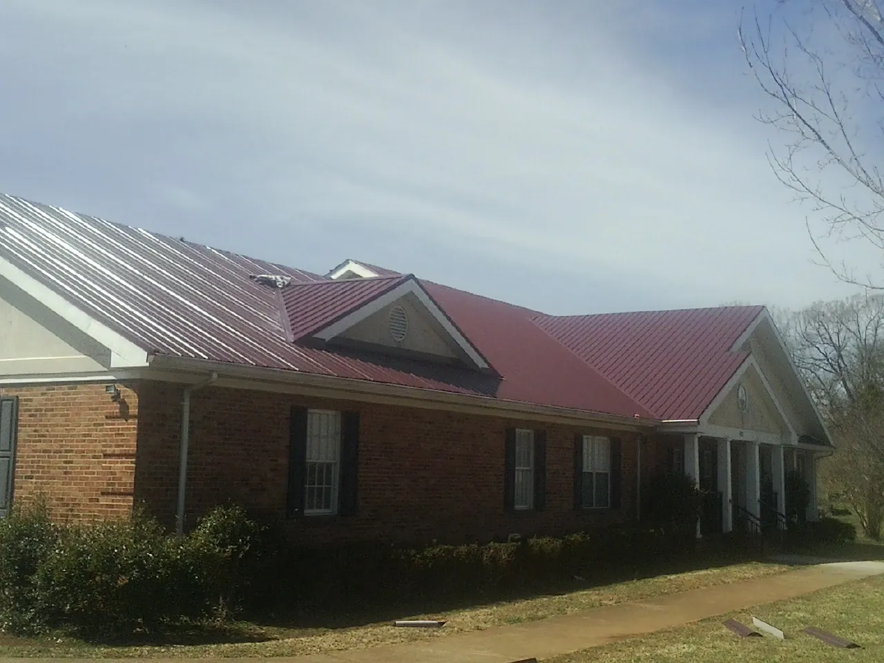 Red metal roof with gabled entries on a long brick building, from a Hail Damage Roof Repair job in Silvis