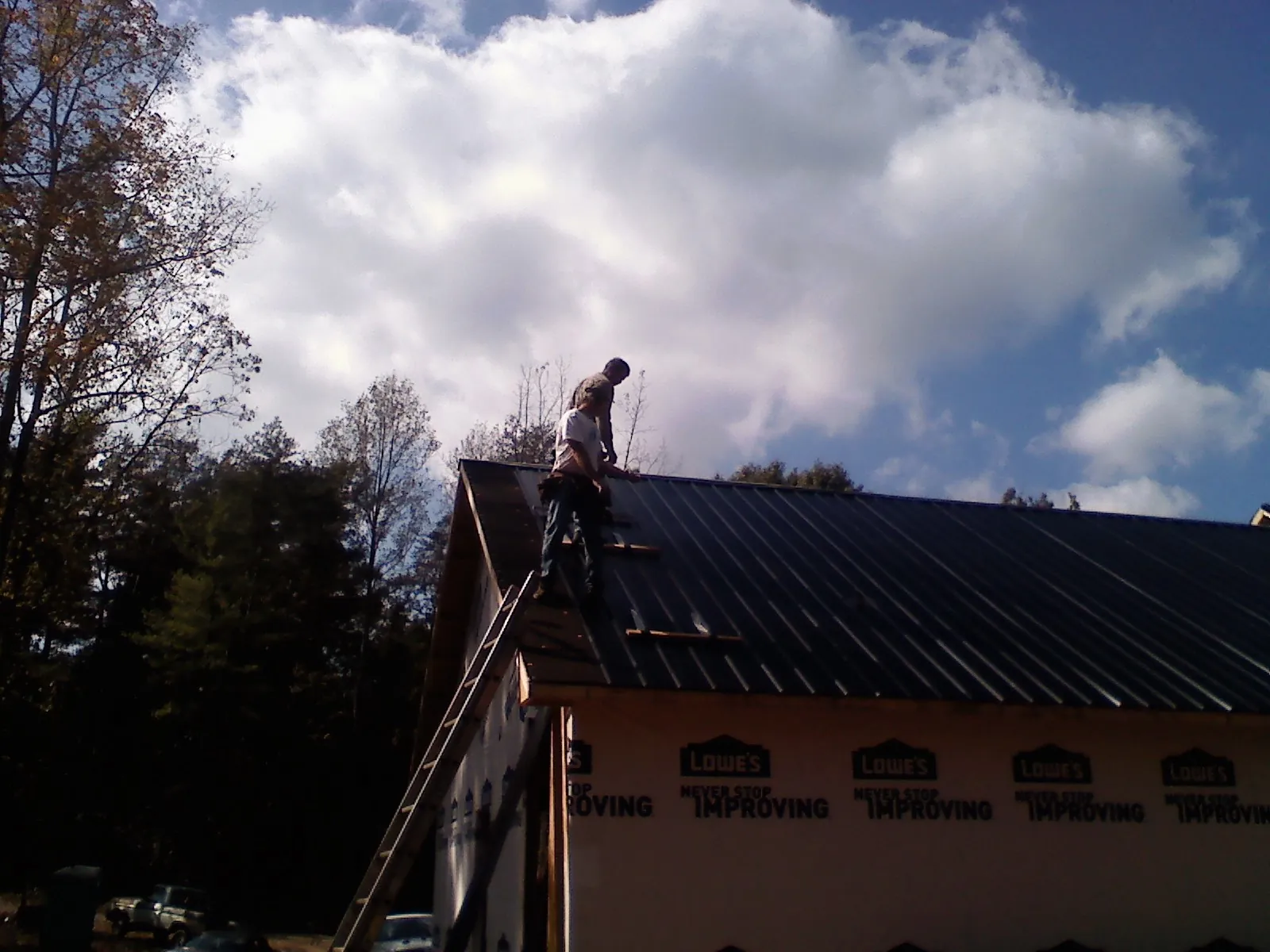 Roofer fastening dark metal panels high against a cloudy sky, from a Roof Inspection job in Silvis