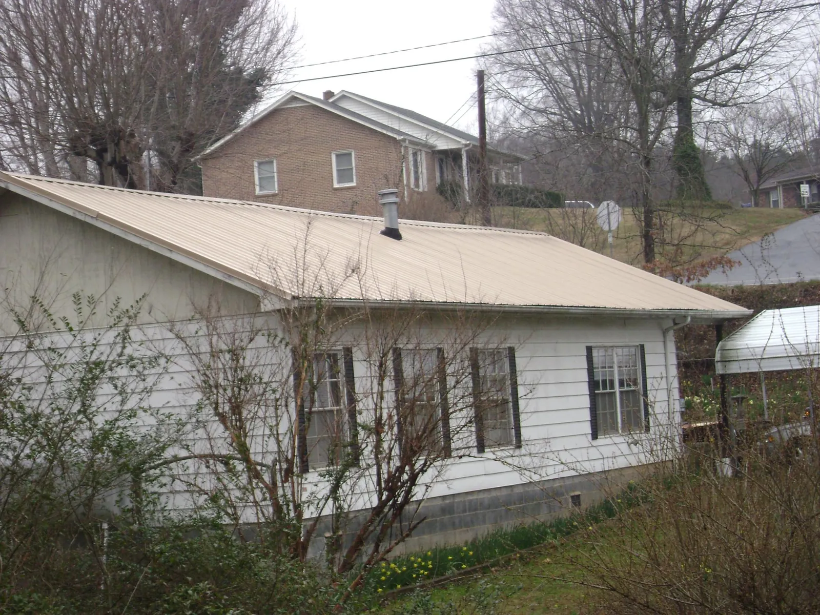 Tan metal roof on a white sided house set into a hillside — Commercial Roofing by Roofing Brothers in Silvis