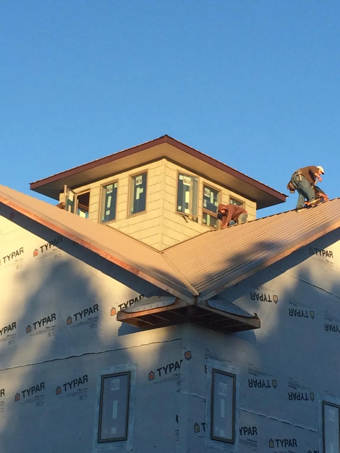 Roofers working around a rooftop cupola on a new metal roof at sunset — Roof Waterproofing in Silvis by Roofing Brothers